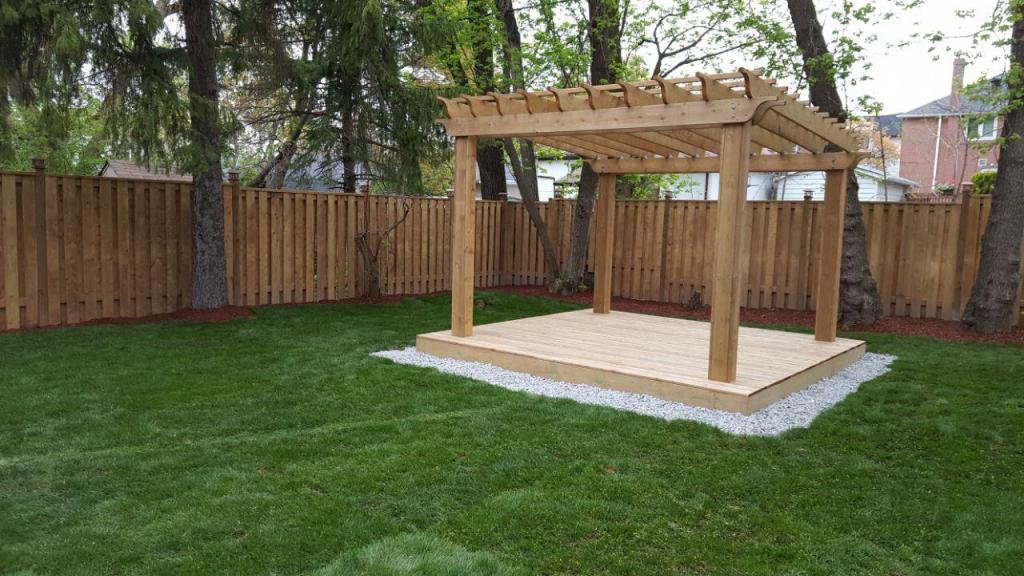Wood pergola structure on concrete slab near fence